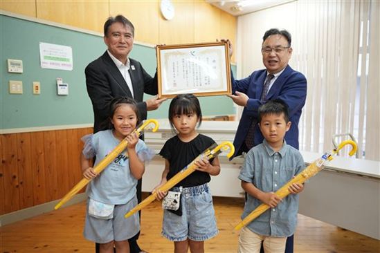 寄贈された傘を持つ児童の代表と、村井博敏理事長、中島教育長